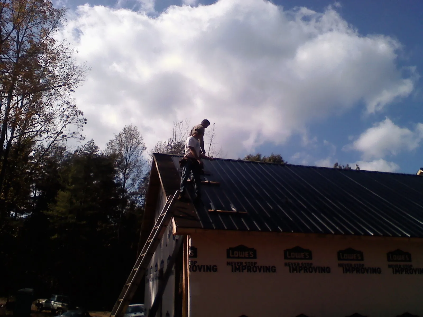 Roofer fastening dark metal panels high against a cloudy sky, from a Roof Inspection job in Blakely Island