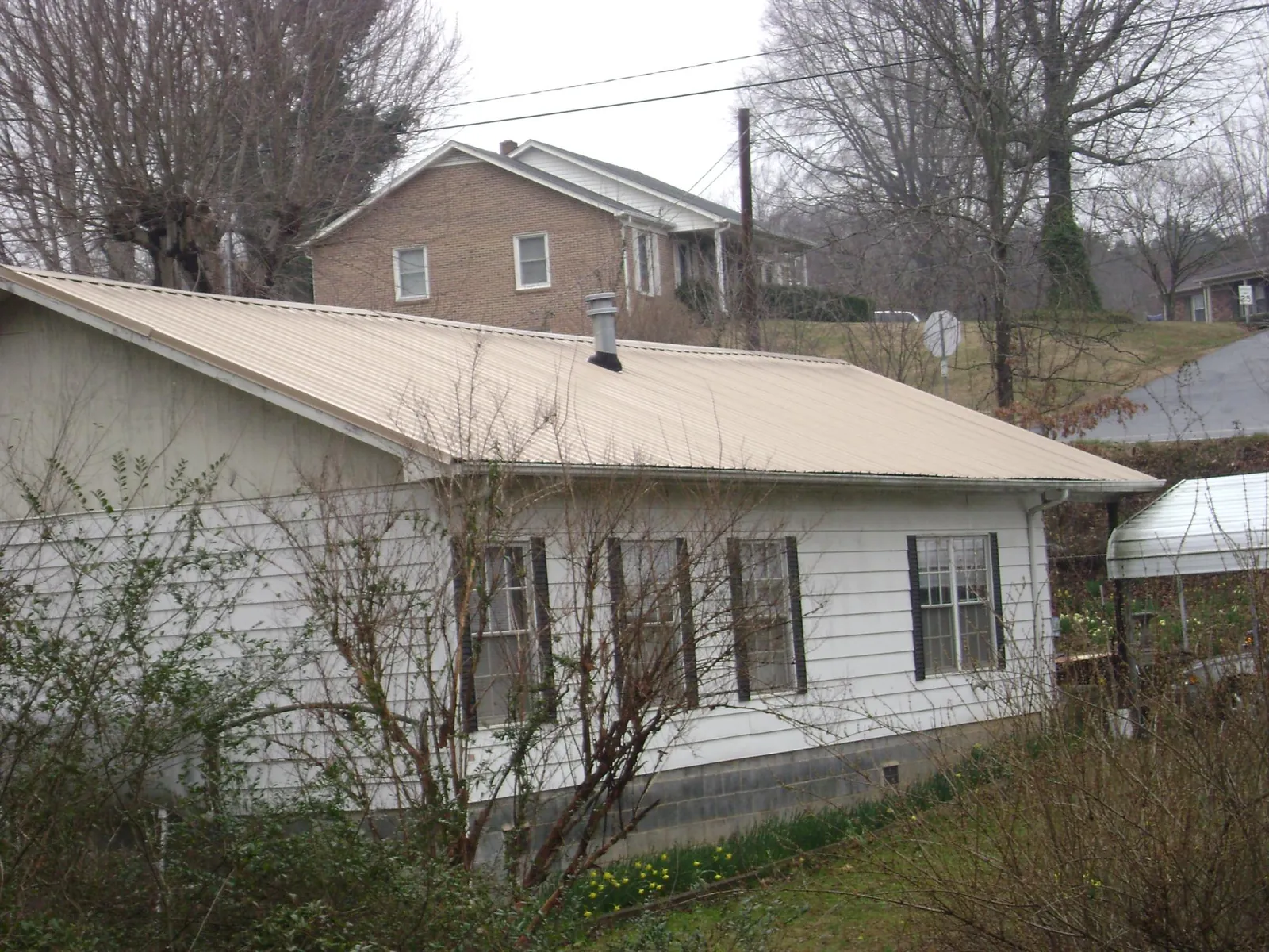 Tan metal roof on a white sided house set into a hillside — Commercial Roofing by Roofing Brothers in Blakely Island